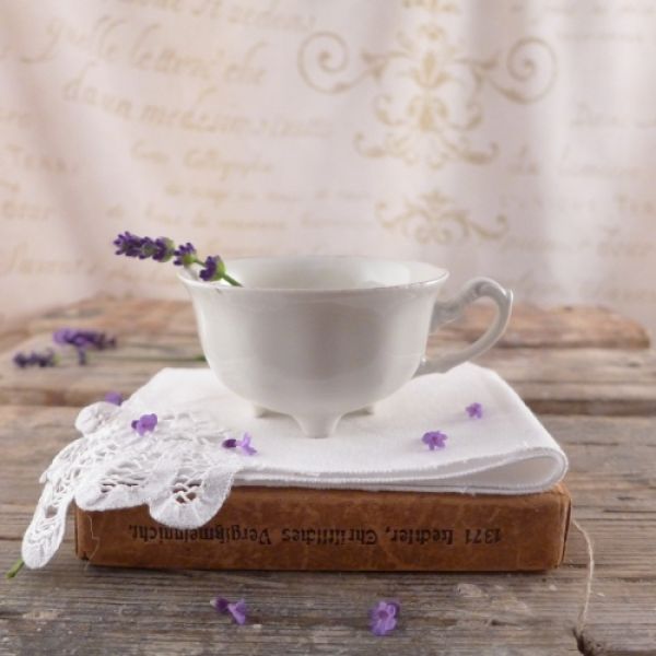 Urocza, malutka filiżanka w kolorze kości słoniowej na nóżkach.