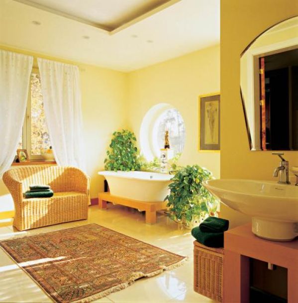 Wolnostojąca wanna została ustawiona przy okrągłym oknie-bulaju, wśród zieleni.