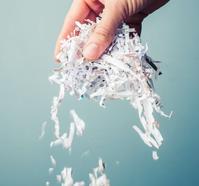 kobieta wkłada kartki papieru do niszczarki dokumentów