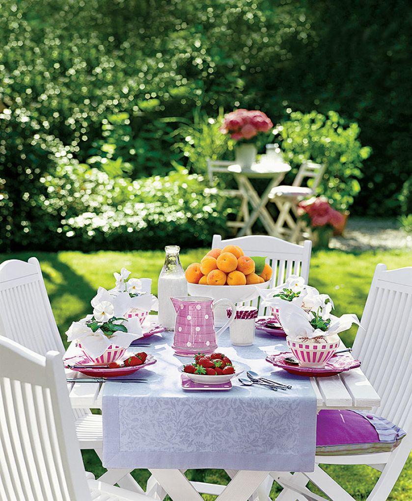 Pastelowe kamionkowe naczynia, biały obrus i proste białe krzesła.