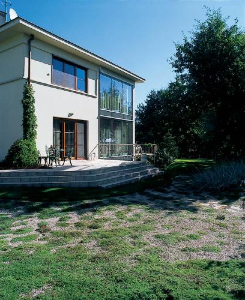 Na tarasie stoją meble ogrodowe. Nad rzeczką, pośród traw