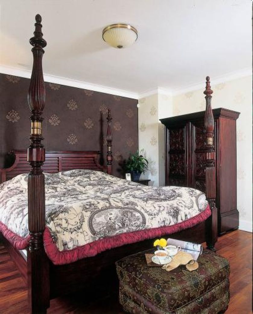 Inspirowane Orientem łóżko z kolumienkami i rzeźbiona szafa nadają sypialni kolonialny styl.