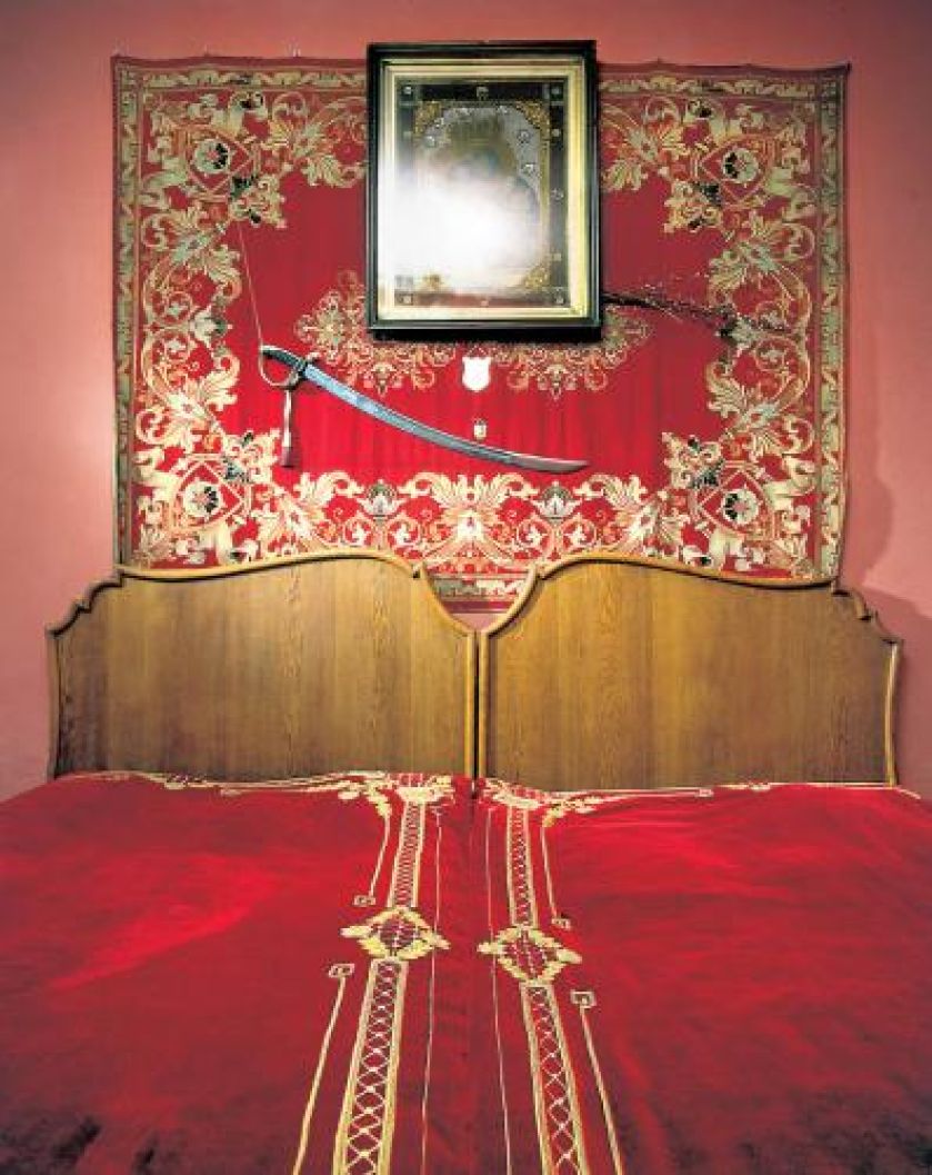 Nad łóżkiem wisi obraz Matki Boskiej, a pod nim szabla.