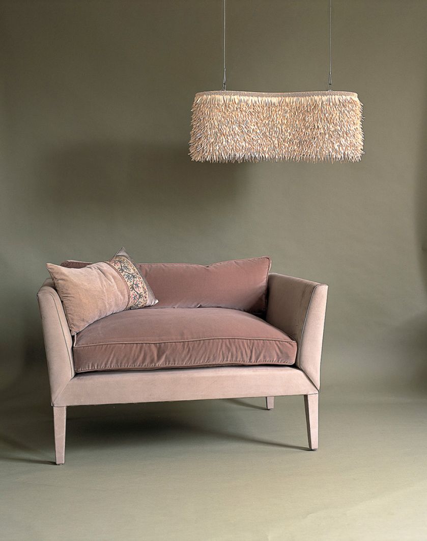 Sofka w pudrowym różu z puchatą lampą.