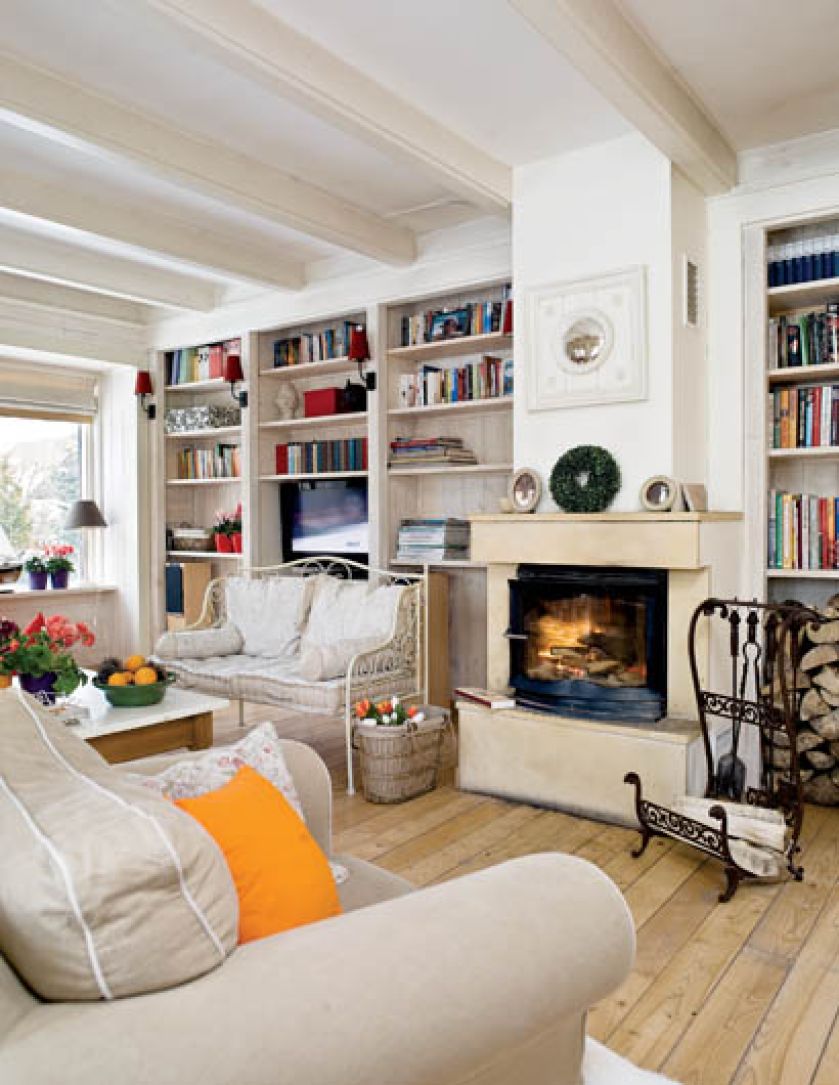 Nad paleniskiem w kominku wisi weneckie lustro. Obok kominka stoi kuta ławka z kremowymi poduchami.