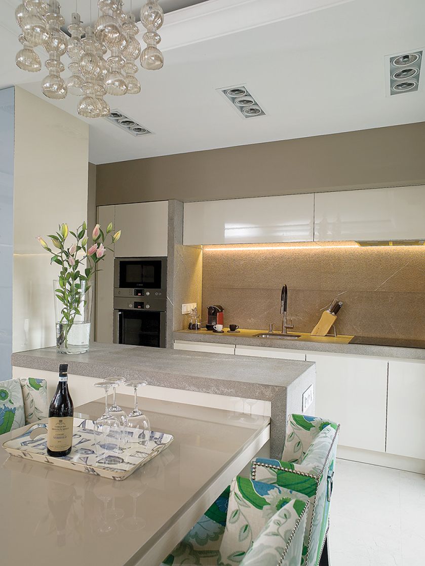 Chłodny kamień i fronty na wysoki połysk ocieplaja krzesła obite lnem marki Christopher Farr.