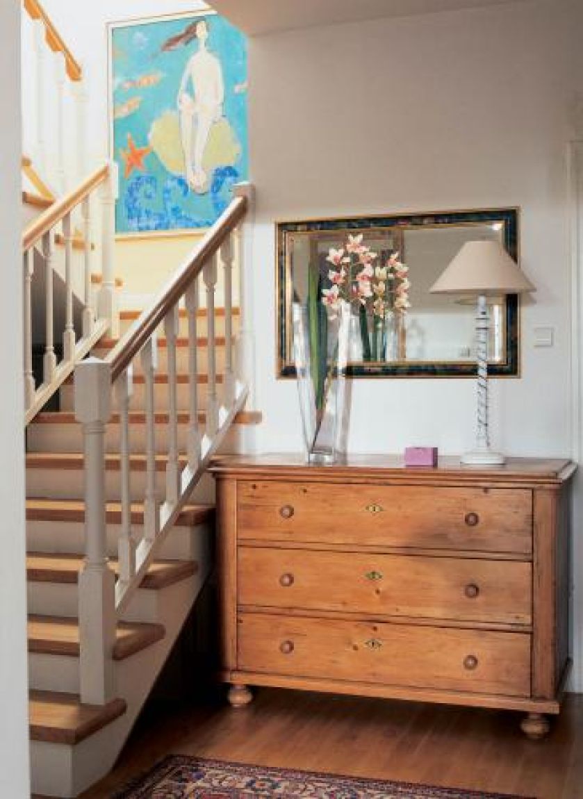 Obok schodów stoi drewniana komoda. Jak szczęśliwie urządzić dom?