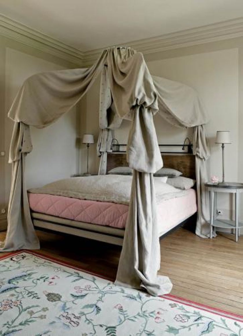 Przy łóżku z baldachimem stoją stoliki i lampki.