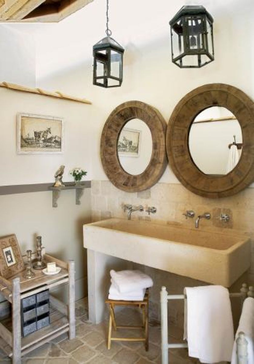 Kamienna podłoga i umywalka komponują się z drewnianymi ramami luster i lampionami.