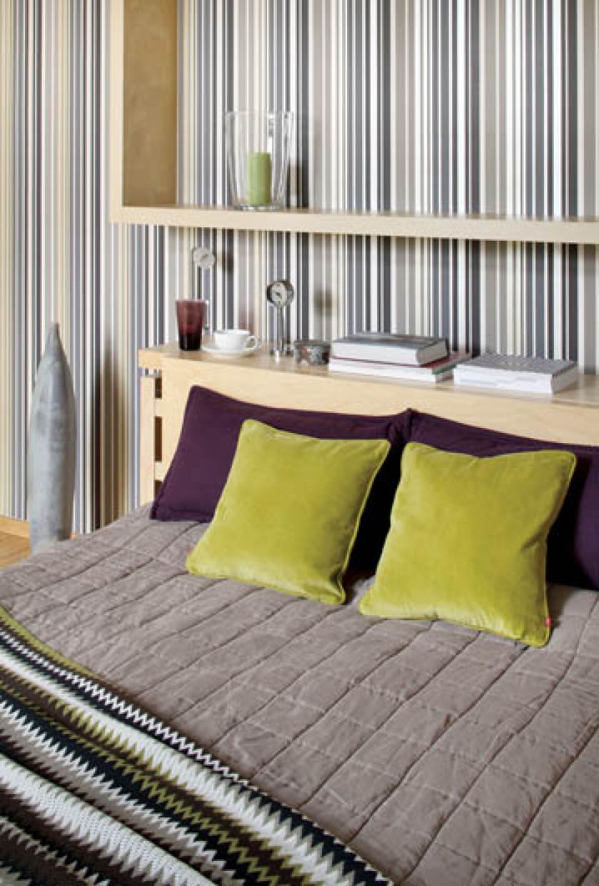 Zielone i fioletowe poduchy oraz tapeta w paski ożywiają sypialnię.