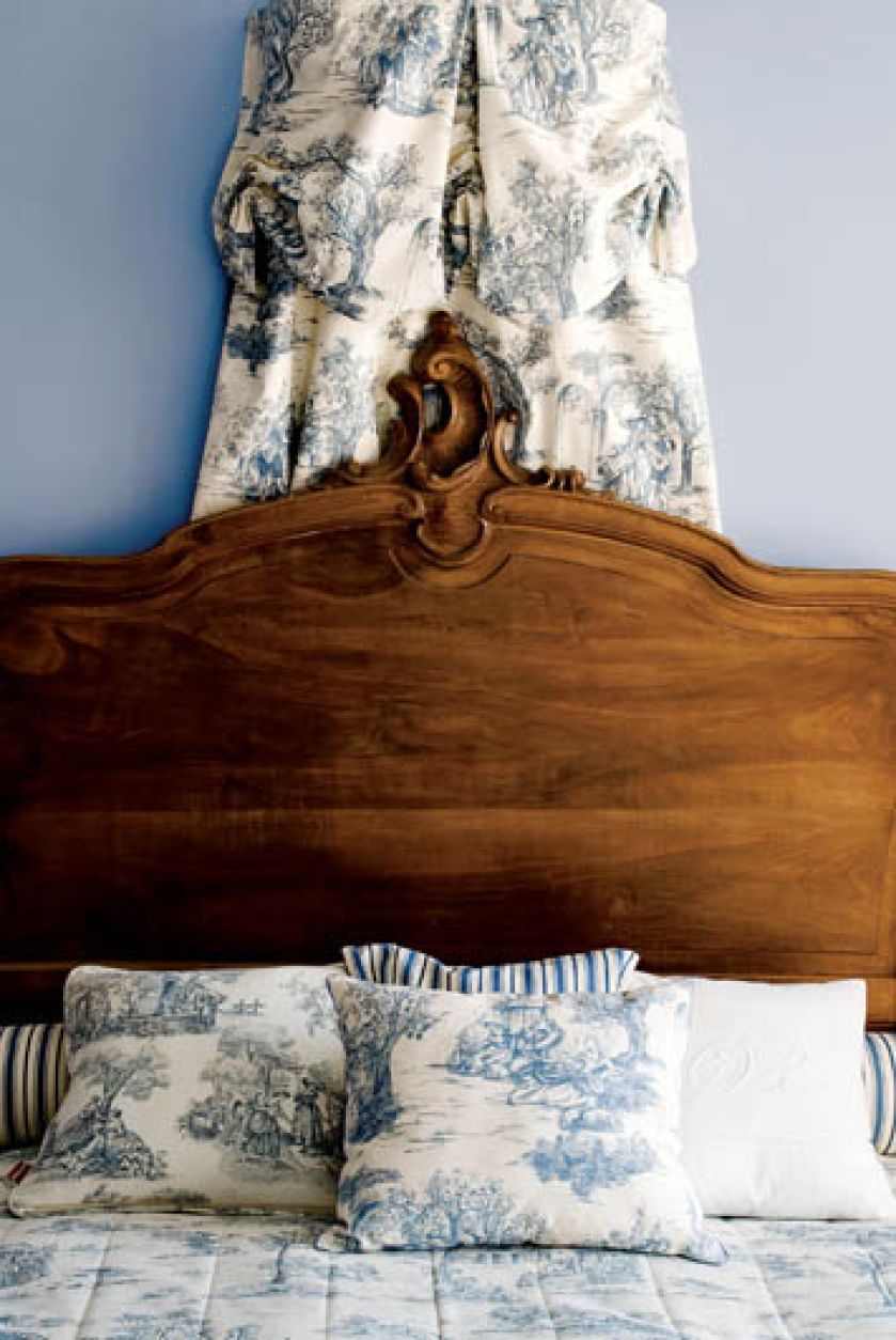 Rzeźbione wezgłowie zabytkowego łóżka, nad nim minibadachim z toile de jouy.