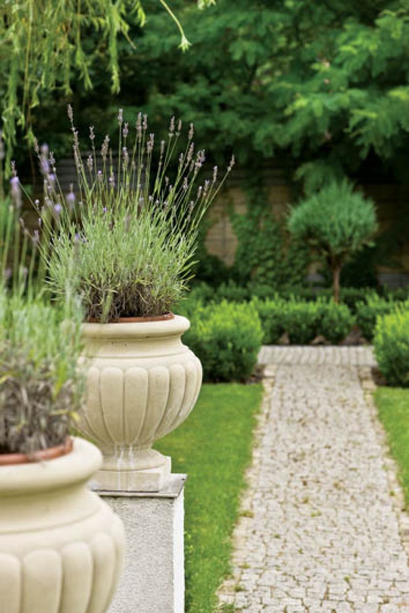 Ogrodowi klasyczny charakter nadają stylizowane na antyczne amfory donice i wysypane żwirem proste alejki.