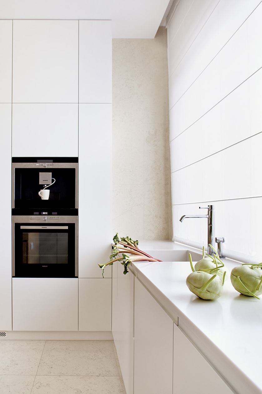 Na podłodze leży wapień perlino bianco. Matowe szafki zestawiono z wyspą-stołem z szarzonego dębu. Sprzęt