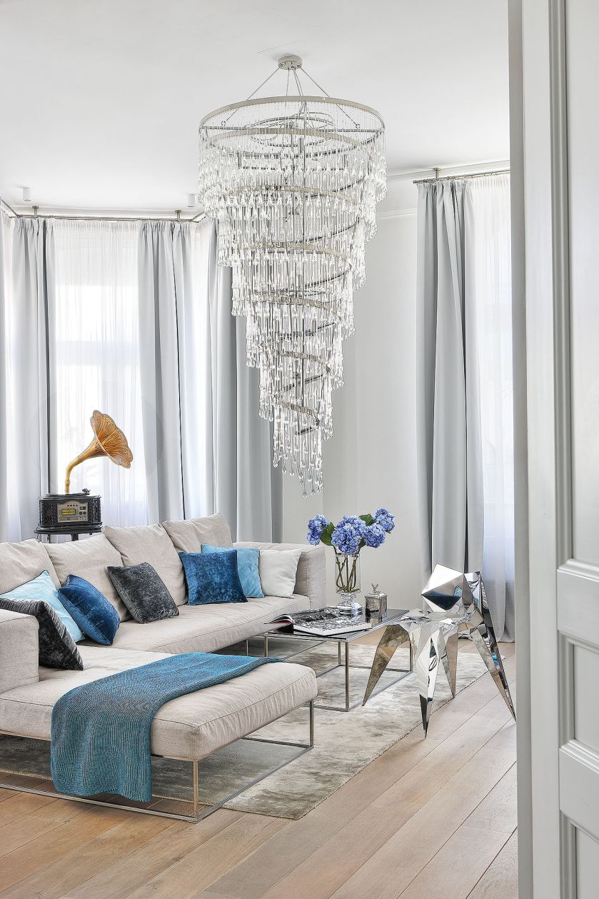 Szklany żyrandol pochodzi z firmy Ochre, sofa Living Divani. Krzesło z polerowanej stali, ręcznie wykańczane