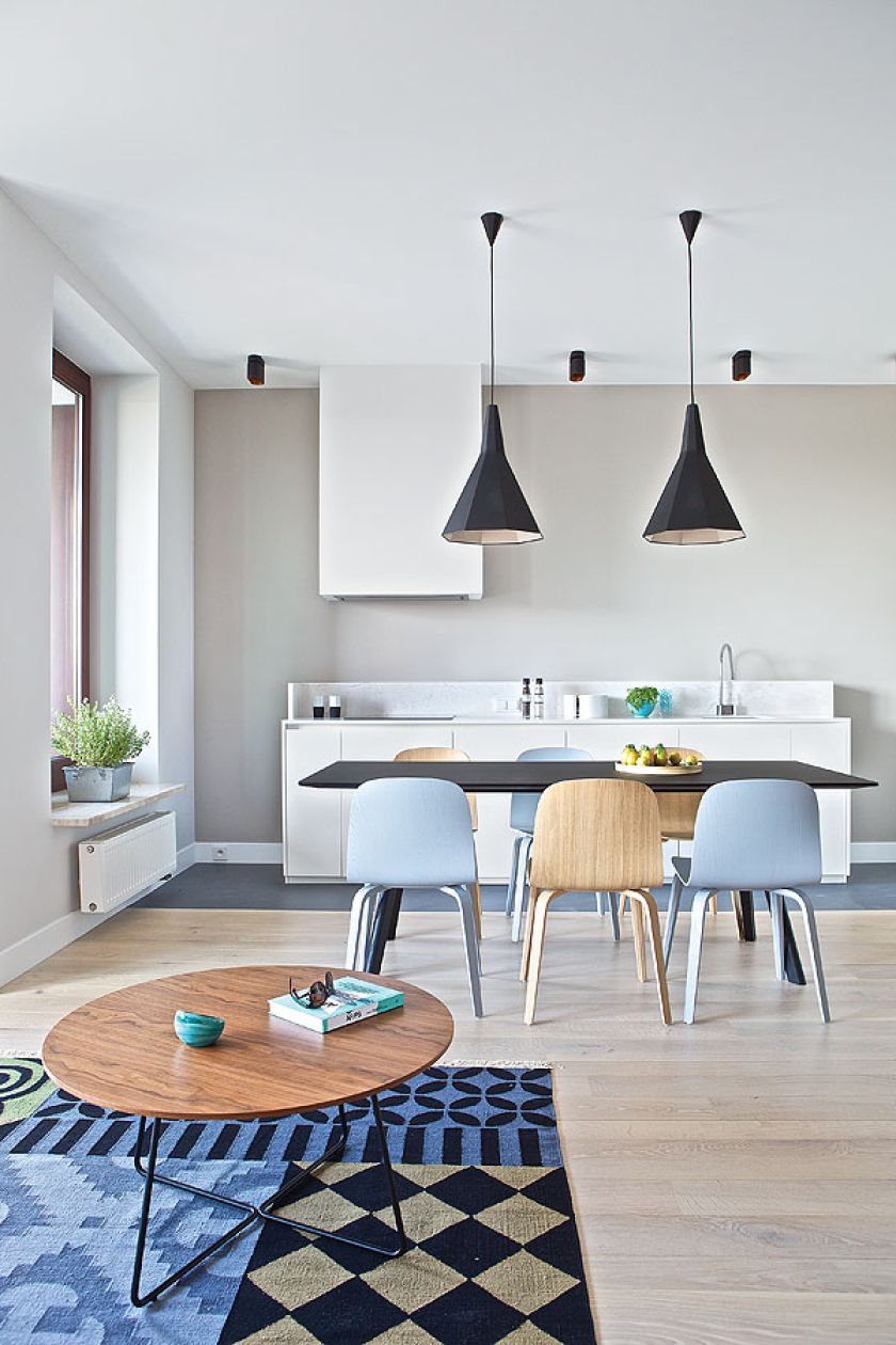 Kuchnia urządzona na biało, ale ciepły ton nadają jej nowoczesne krzesła w kolorze naturalnego drewna i gołębiego błękitu.