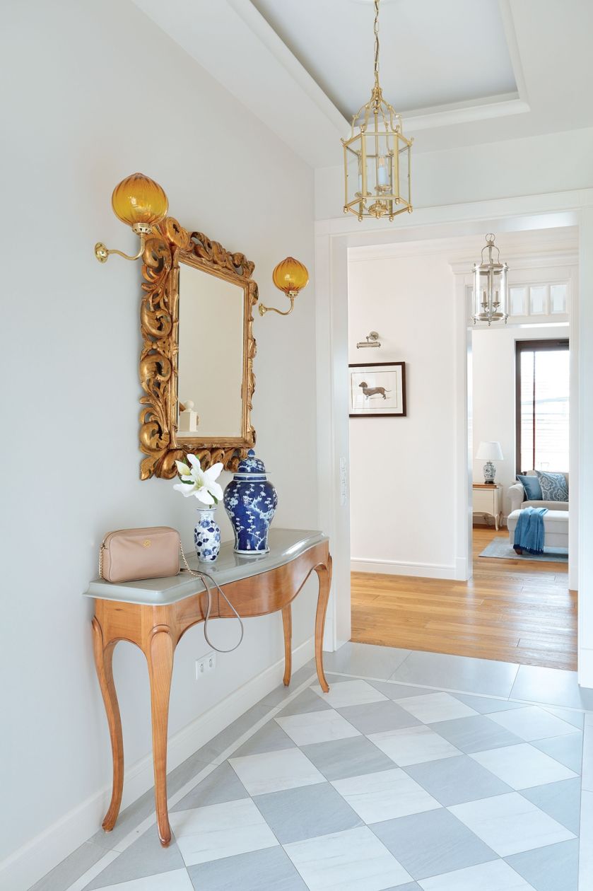 Lustro w ręcznie rzeźbionej złoconej ramie to prezent od rodziców. Pani domu dobrała do niego złociste kinkiety z dmuchanego