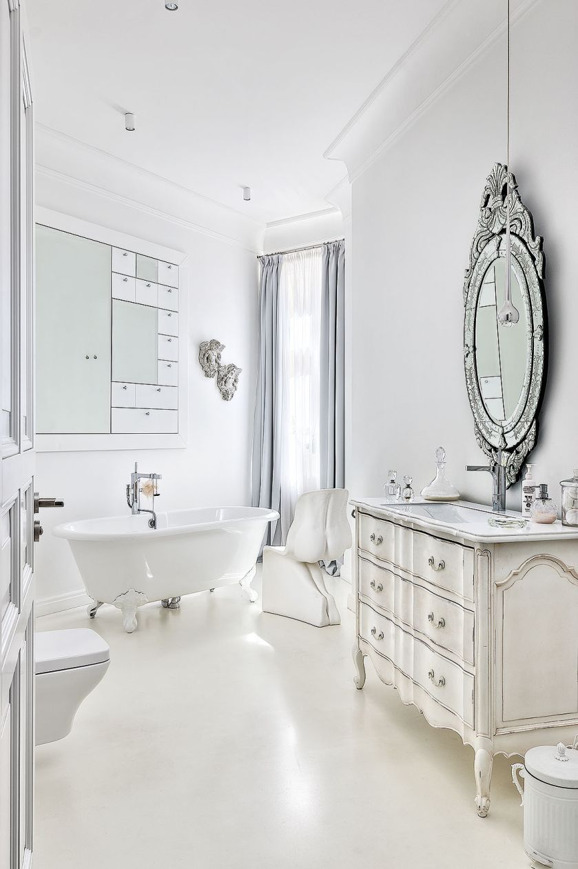 W łazience mieszają się elementy stylowe z dizajnerskimi: obok wanny na ozdobnych nóżkach przezroczysty stołek