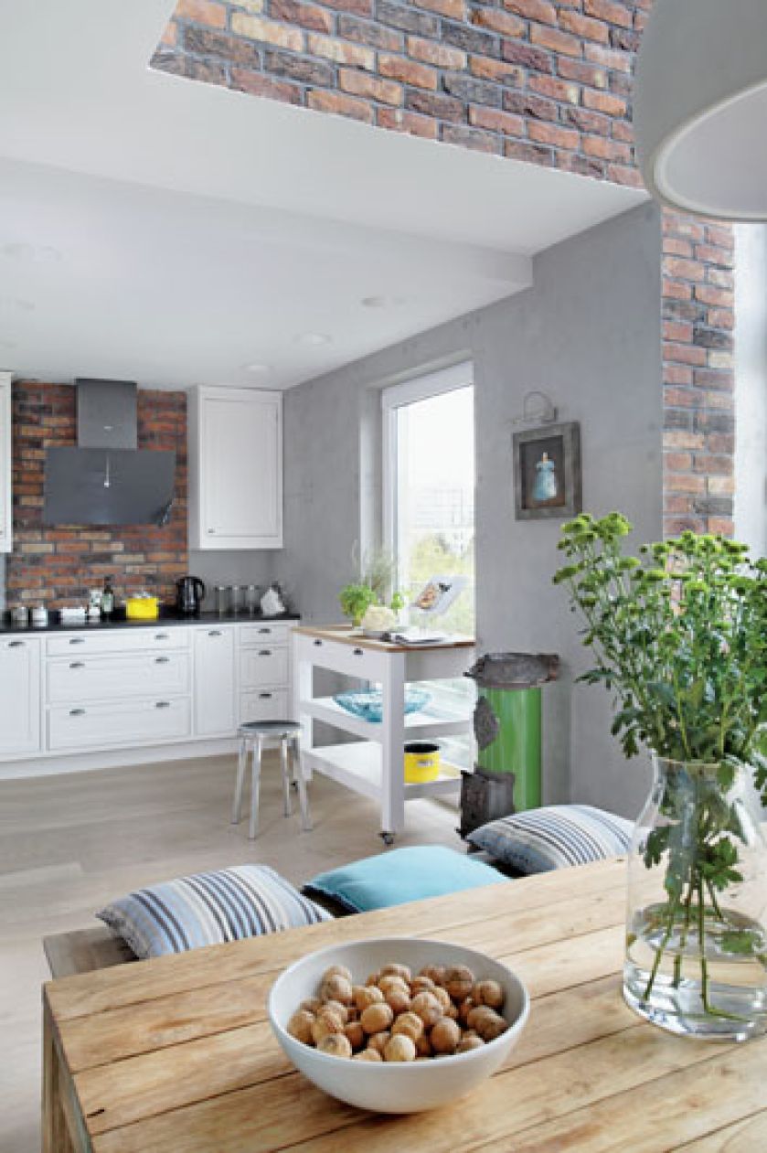 Do tradycyjnie wypalanej, holednerskiej cegły pasuje surowy drewniany stół. Nad kozą wisi obraz warszawskiej malarki