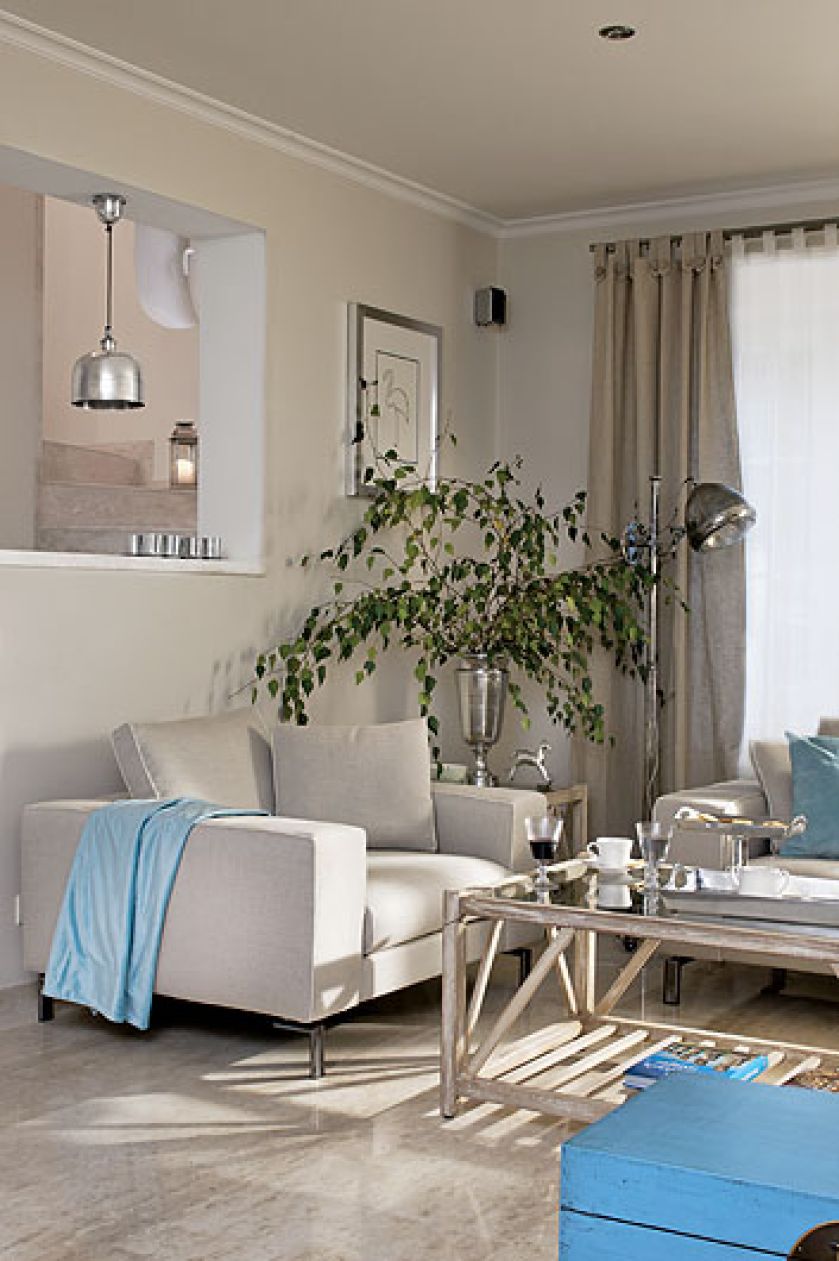 Kremowe sofy, fotele i kawowy stolik z turkusowymi dodatkami.