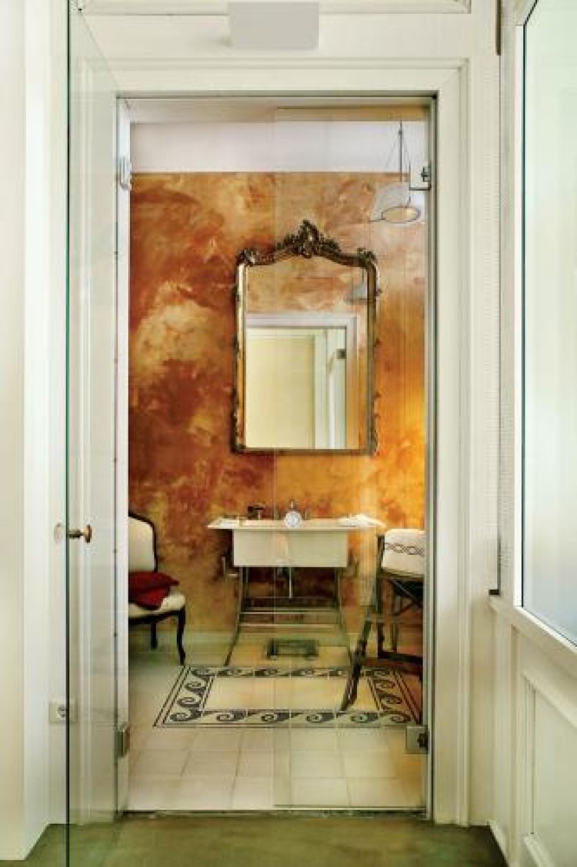 Łazienkę od sypialni oddzielają wysokie szklane drzwi. Stiuk, mozaika, francuskie lustro, stary fotel, biblioteczne schodki