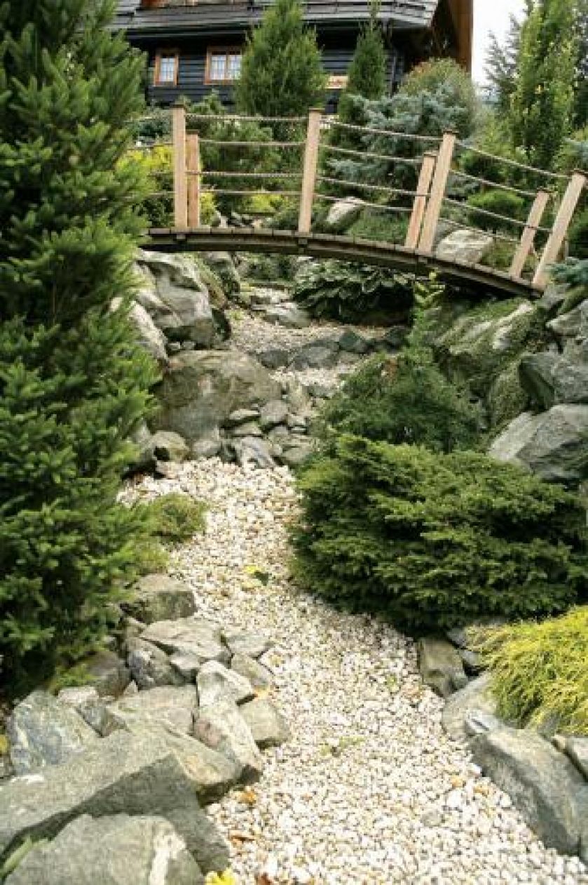 Mostek nad kamiennym strumieniem. Tarasowy ogród otoczony naturą