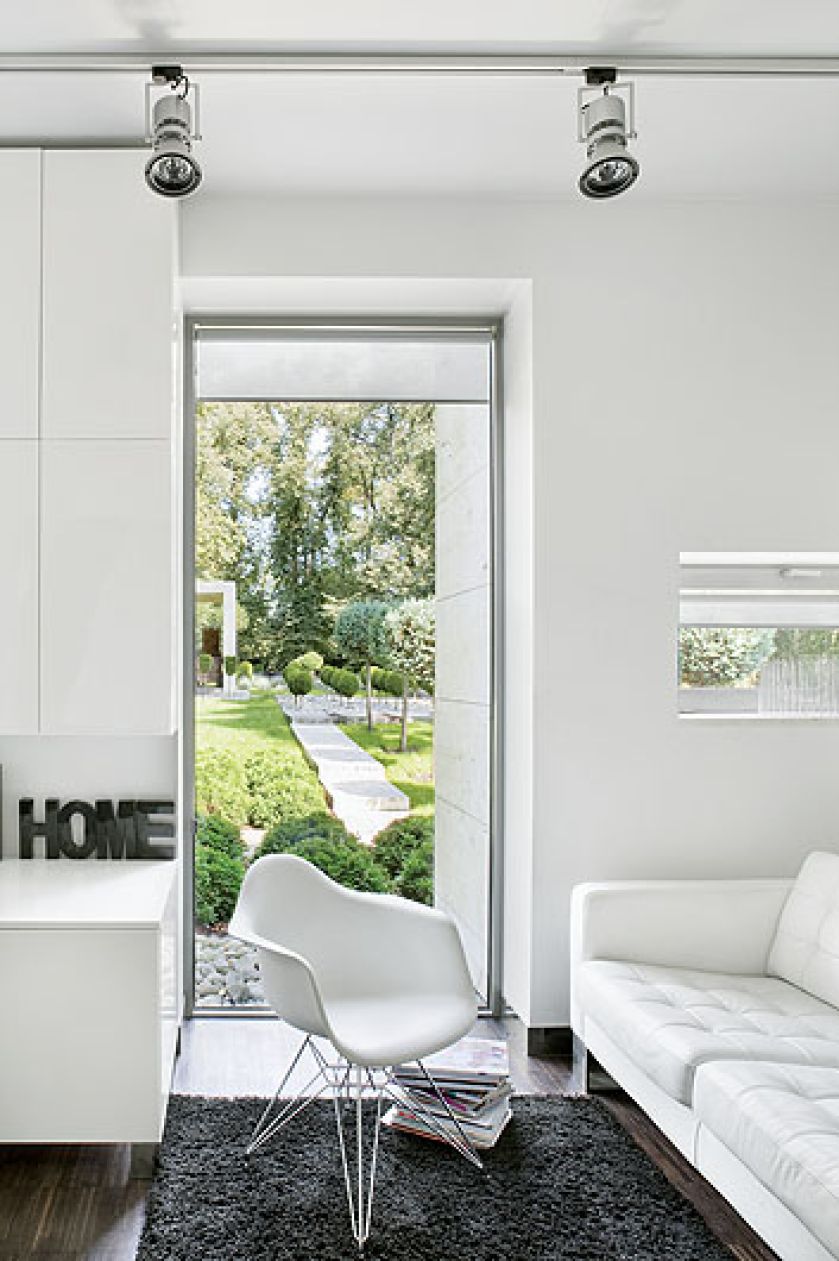 Skórzana kanapa i widok na ogród. A tam trawertynowy chodnik, kule z tui wśród białych kamieni i przystrzyżone cisy.