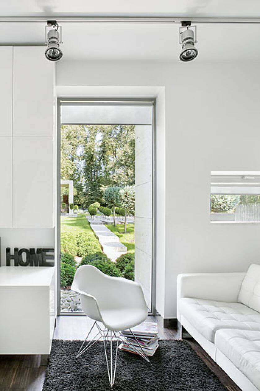 Skórzana kanapa i widok na ogród. A tam trawertynowy chodnik, kule z tui wśród białych kamieni i przystrzyżone cisy.