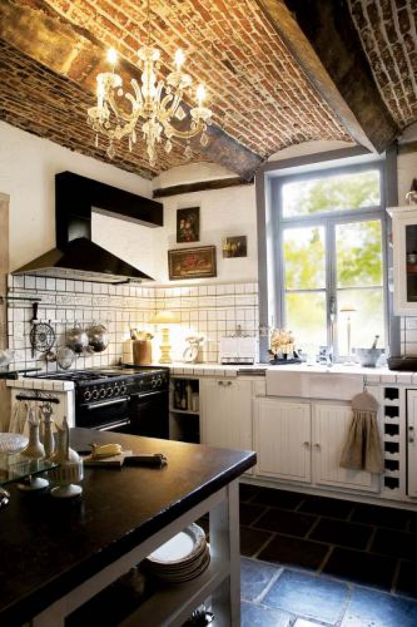 W kuchni wenecki żyrandol na tle ceglanego sufitu, superpiecyk La Cornue i stół z bazaltowym blatem. Do tego dużo