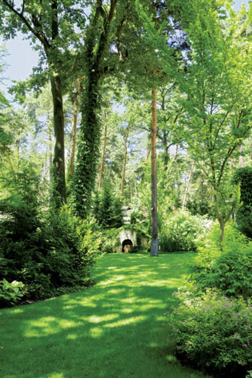 W oddali widać kamienną ziemiankę. Ogród z leśną ziemianką