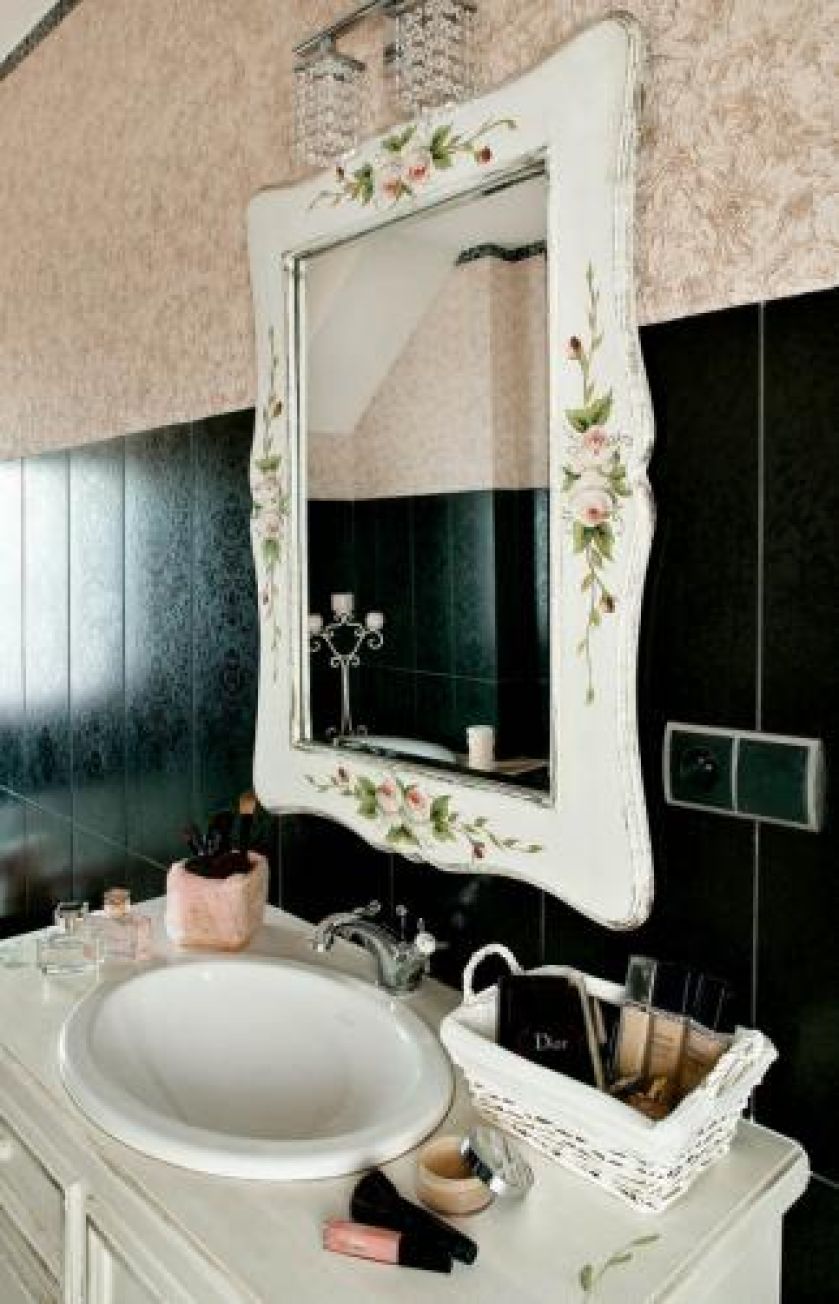 Nad umywalką wisi lustro w zdobionej ramie.