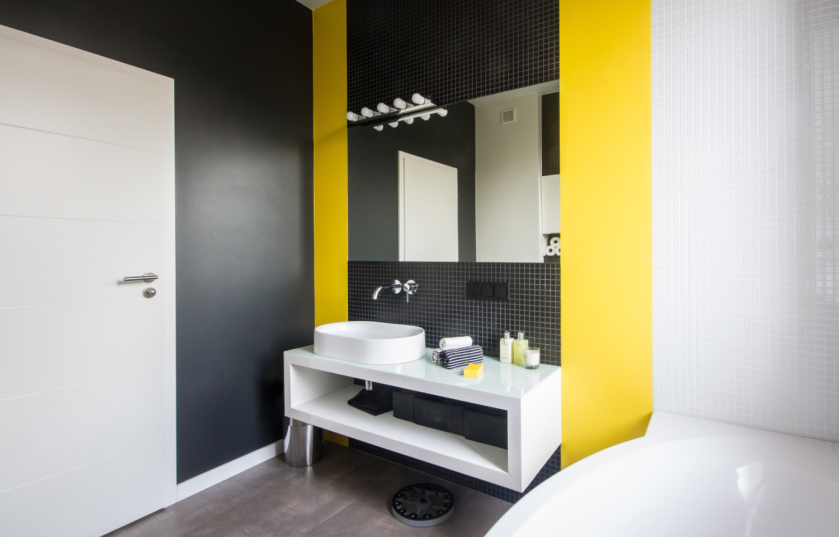 Nowoczesną i monochromatyczną aranżację łazienki dynamizują żółte pasy między płytkami.