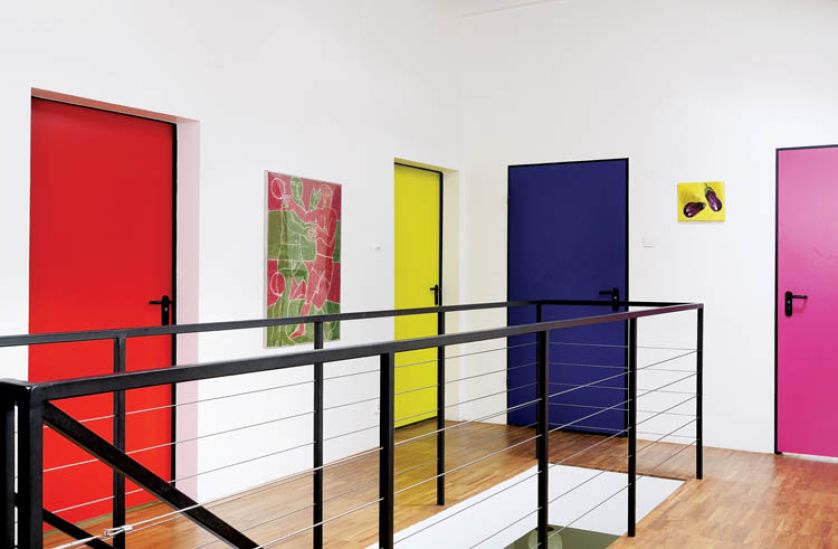 Śnieżnobiałe ściany i wielokolorowe drzwi aż fosforyzują barwą.