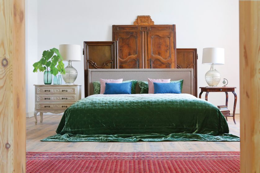 W SYPIALNI ZA WEZGŁOWIEM ŁÓŻKA STOI DEKORACJA Z DRZWI POCHODZĄCYCH Z BAROKOWYCH SZAF. PO PRAWEJ STOLIK DO GRY W