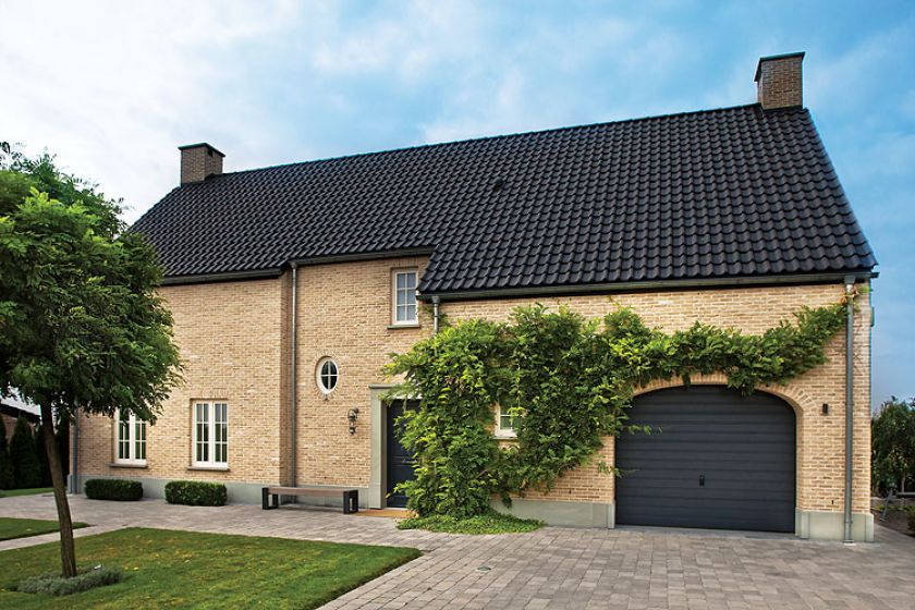 Ceglana elewacja, czarny spadzisty dach i minimalistyczny ogród.