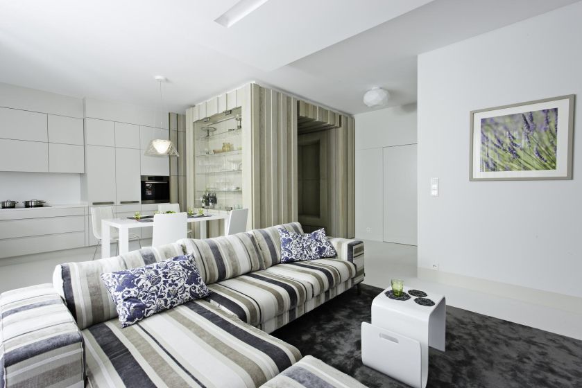 Ciekawa ściana wykończona drewnem jest kontynuacją przedpokoju. Białym akcentem jest fantazyjnie wygięty stolik kawowy.