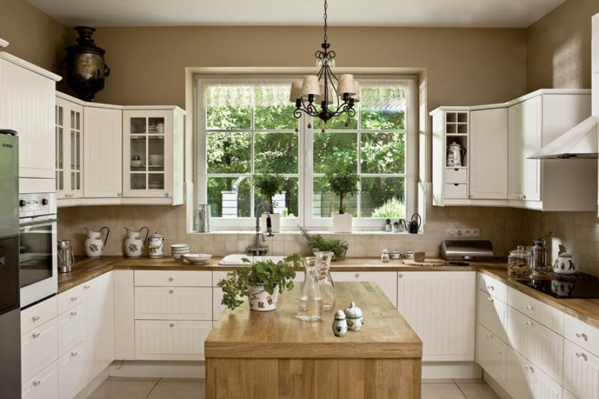 Do kuchni w podmiejskim domu pasują proste białe meble z drewnianymi blatami.