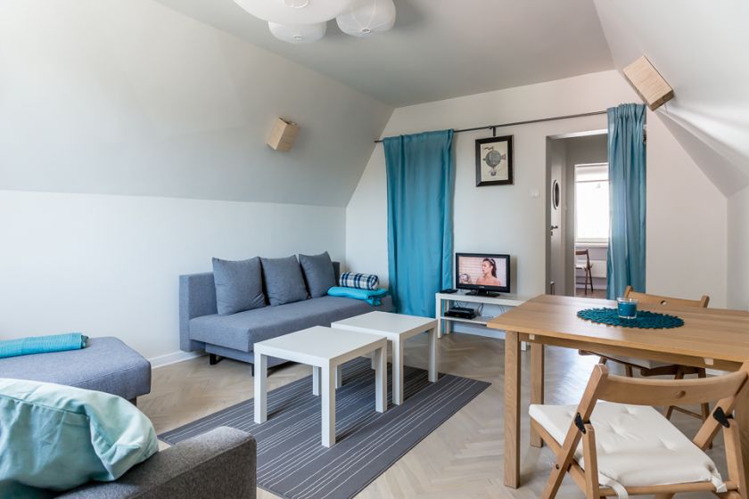 Dwie kanapy, dwa stoliki kawowe oraz większy drewniany stół ze składanymi krzesłami.