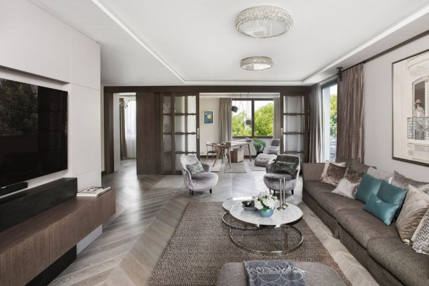 Stonowaną kolorystykę salonu w beżach i szarościach ożywiają błękitne motywy: sukienka kobiety w kapeluszu na