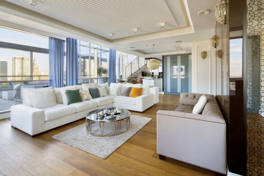 W SALONIE: DĘBOWA PODŁOGA Z ETSSO. SOFA PIKOWANA, STOLIK KAWOWY I KINKIETY MARKI EICHHOLTZ. BIAŁA NAROŻNA SOFA – OLTA.