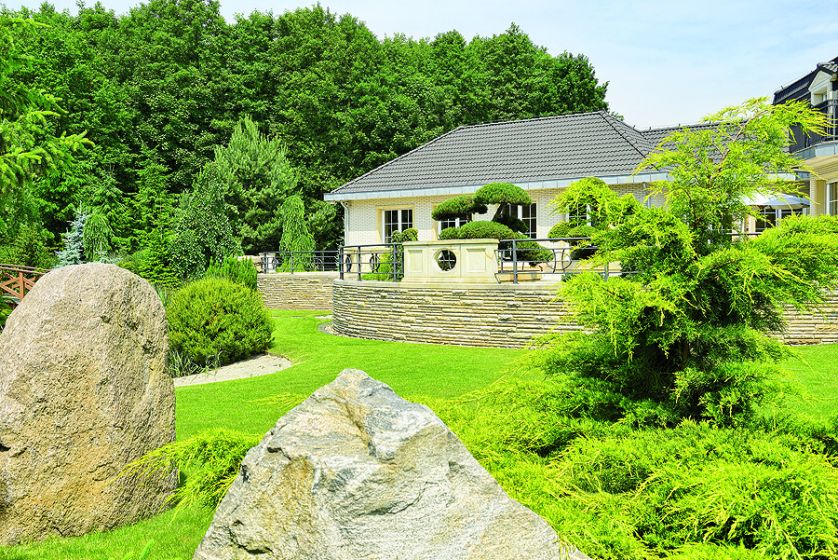 Wielkie głazy ozdabiają ogród. Zieleń, kamień i woda