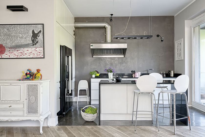 W kuchni czarna lodówka, podłoga z samopoziomującego się betonu i wyspa z polerowanego kamienia.