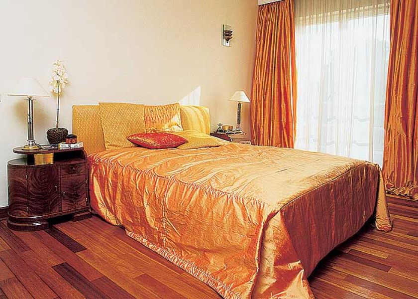 Cieply pomarańcz kapy na łóżku i zasłon ładnie harmonizuje z podłogą.