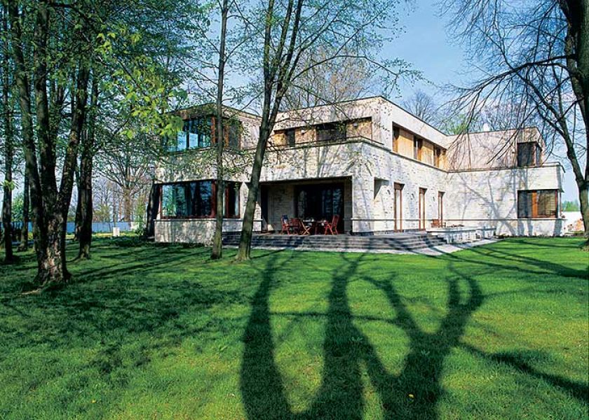 Nowoczesna willa otpczona starymi drzewami.