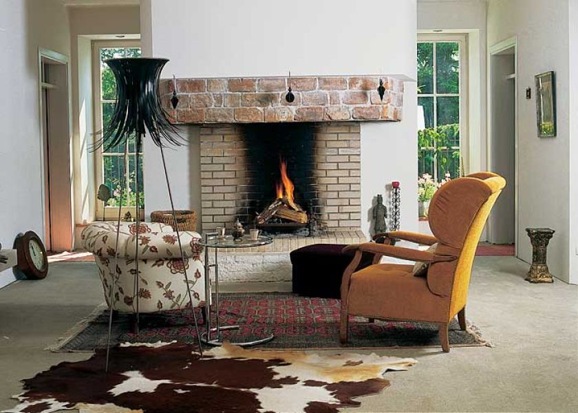 Okna w ścianie za kominkiem, przez ktore widać las, i otwarte palenisko sprawiają, że możemy poczuć się prawie jak