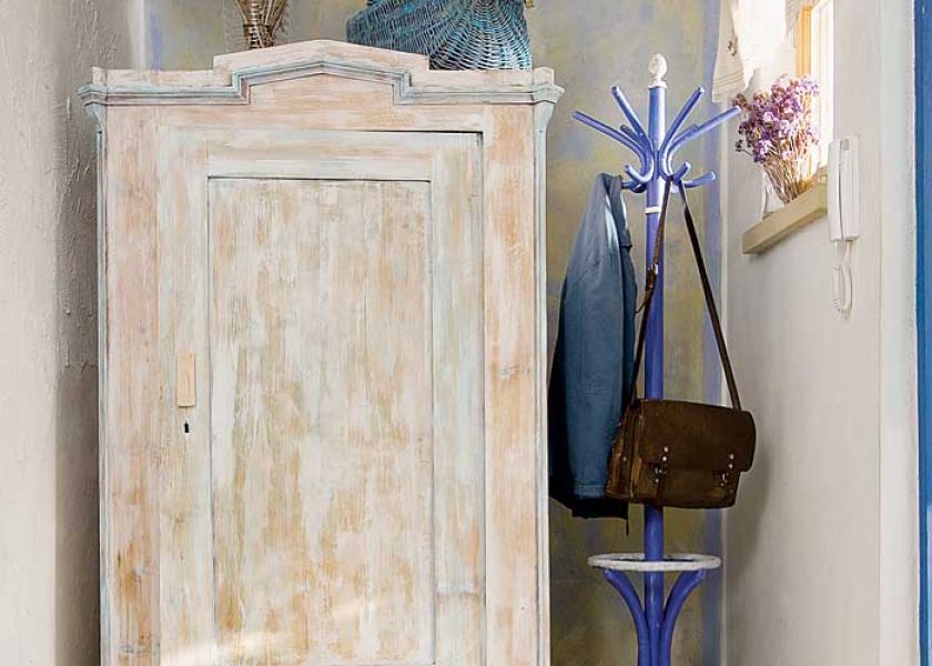 Przetarta farbą akrylową drewniana szafa i niebieskie akcenty przywodzą na myśl styl prwansalski.