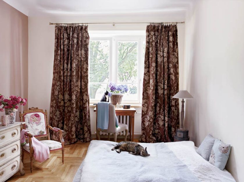 W sypialni biel i ecru rozpraszają brązowe zasłony i delikatne róże.