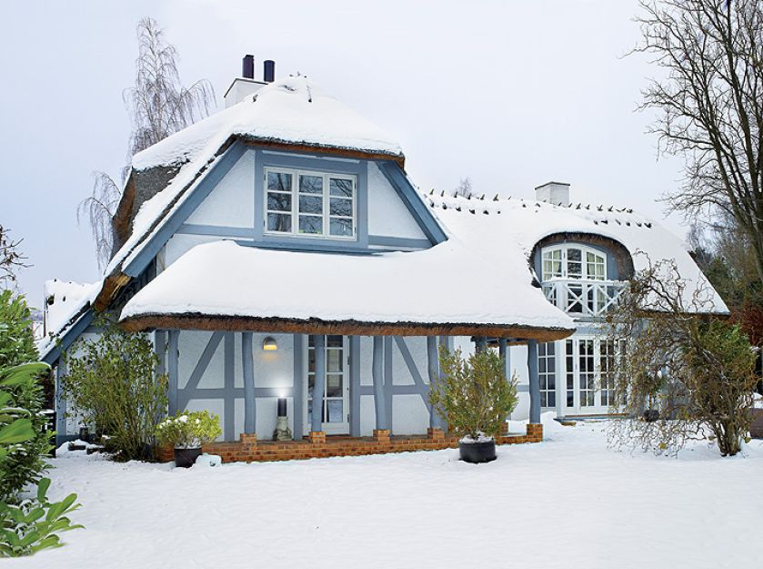 Stuletni dom z dachem krytym strzechą i szarym szkieletem.