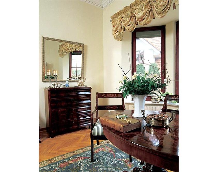 Nad komodą wisi lustro w zdobionej ramie.