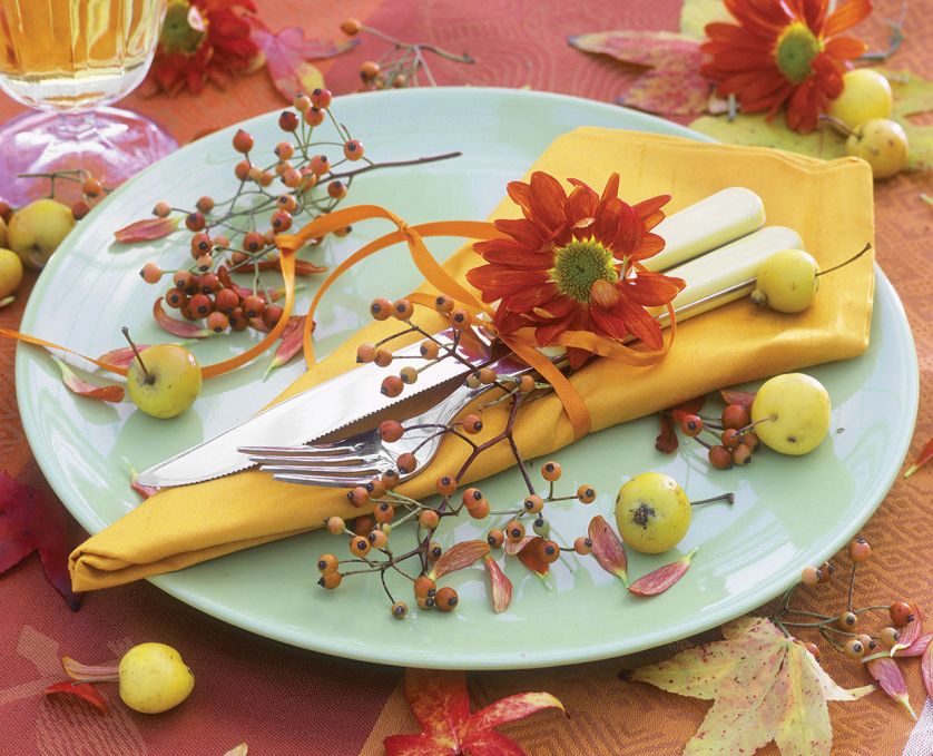 Jesienny miszmasz na stole: kwiaty, gałązki jarzębiny, małe jabłuszka i kolorowe liście