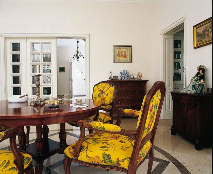 Żółte obicie krzeseł ożywia pełne antyków wnętrze.